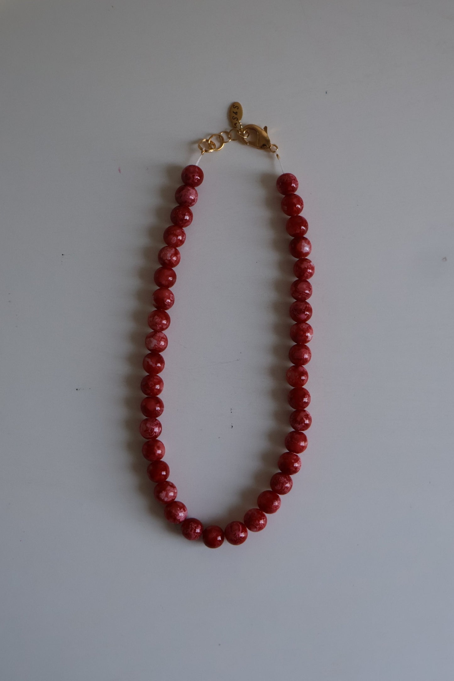 Red beaded necklace with a gold clasp on a white surface