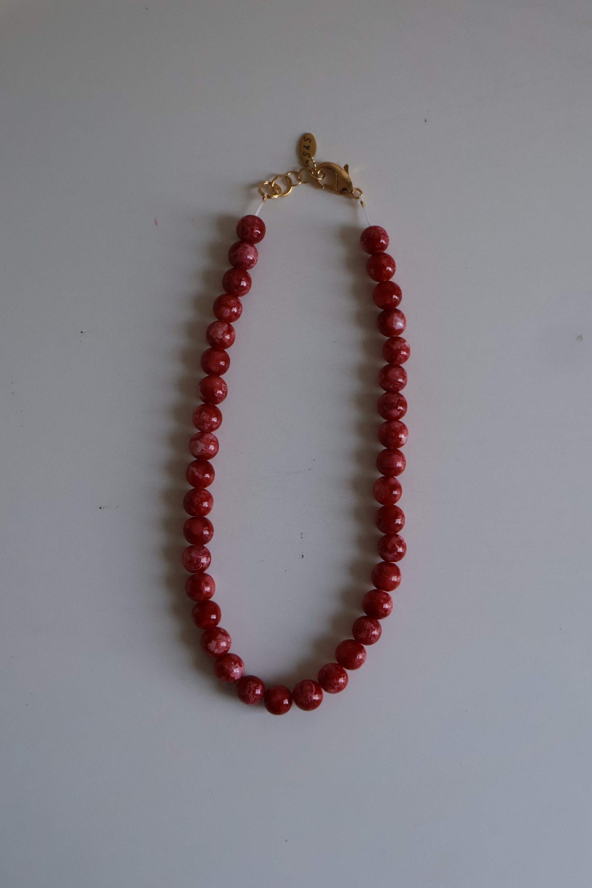 Red beaded necklace with a gold clasp on a white surface