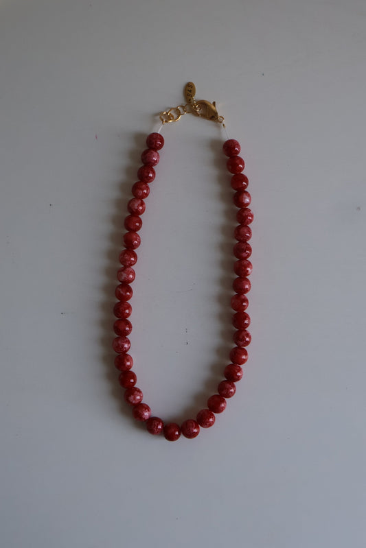 Red beaded necklace with a gold clasp on a white surface